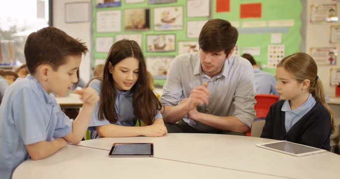 4k, Elementary school teacher with his pupils in classroom using a digital touchscreen tablet. Slow motion.