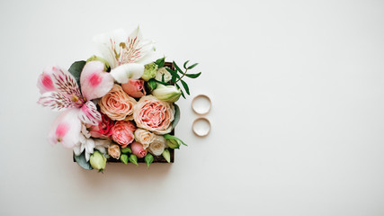 Two golden wedding rings arranged near beautiful and cute flower composition in a little box