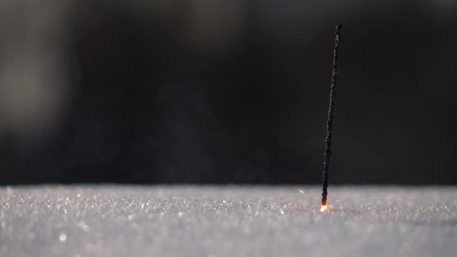 Thin and weak Bengal or Indian light, or sparkler, stick into snow and dying on dark background in slow motion, 240 fps. Pathetic and melancholy image.
