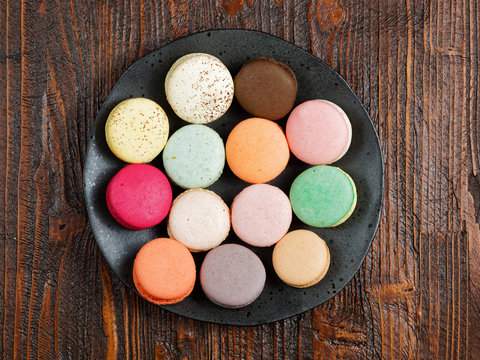 Brightly colored macaroons on a hand-made plate, set on a rustic brown wooden board