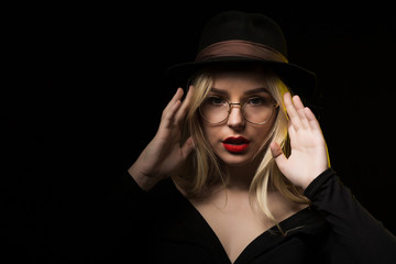 Magnificent young woman wearing black blouse, hat and glasses, posing in the shadow