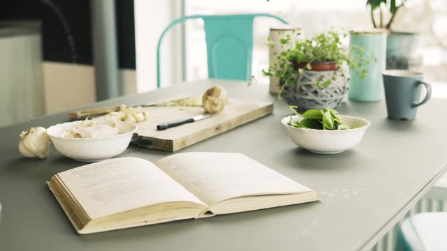 Recipe book, spinach and garlic on a table in kitchen.