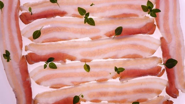 Amazing top view of fresh sliced bacon in rows with basil leaves close up, rotating clockwise. Vibrant natural food background with excellent texture and back light in 4k, 3840x2160, clip.
