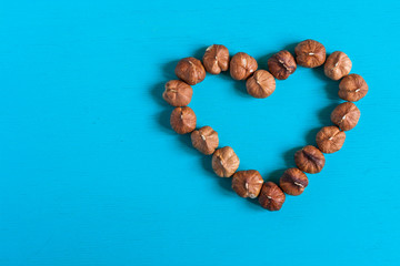 Filbert nuts, lay out in the form of heart on a bright blue painted wooden background.