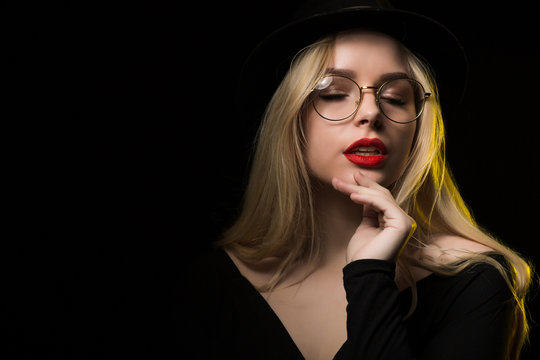 Awesome blonde woman wearing black blouse, hat and glasses, posing in the shadow