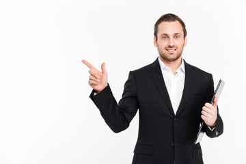 Photo of successful entrepreneur wearing business suit pointing finger aside and posing with documents in hand, isolated over white background copy space