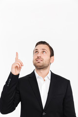 Portrait of smiling entrepreneur having stubble wearing black suit looking upward and pointing index finger up, isolated over white background copy space