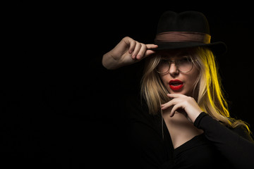 Charming young woman wearing black blouse, hat and glasses, posing in the shadow