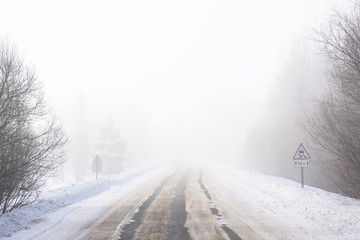 Snow winter landscape. Empty road in fog and Russian slippery road sign