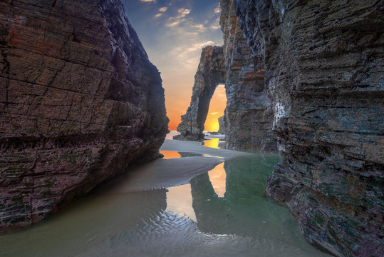 The sky of dawn is reflected in a pool on the beach of As Catedrais