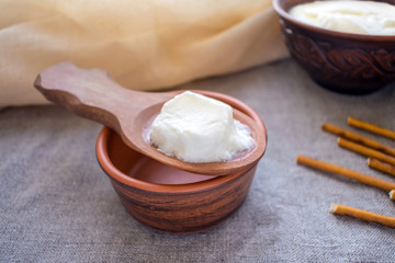 Homemade milk kefir grains on a wooden spoon above a clay bowl of milk kefir. Organic probiotic kephir drink on rustic background. Natural probiotic bulgaros, yoghurt, fermented milk drink