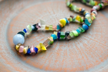 Multi-colored ethnic beads on a brown clay plate. Beads of different bright natural semiprecious stones.Close up Selective focus