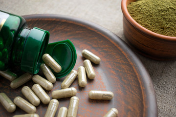 Close up Green capsules, bottle and powder on a clay brown plate on a burlap background. Dietary...
