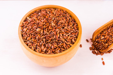 Grains of red rice in a wooden bowl of light table - healthy eating concept, copy space, top view