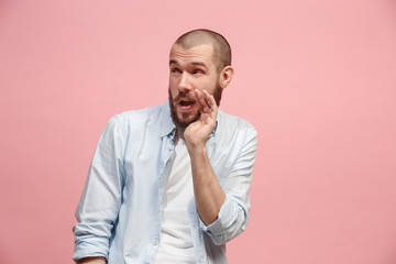 The young man whispering a secret behind her hand over pink background
