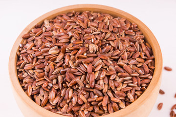 Red rice grains in a wooden bowl on light table close-up - healthy eating concept, copy space, top view