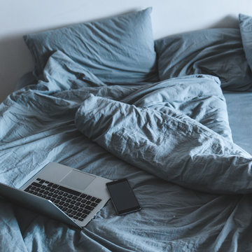 Empty Messy Grey Bed With Laptop. Lifestyle Rest In Bed Concept