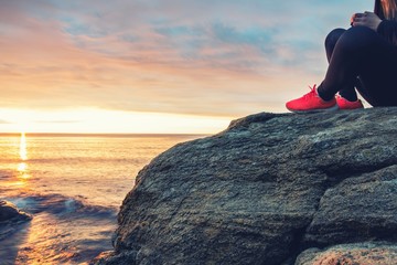 Young girl sitting on a sea rock meeting the morning sun.