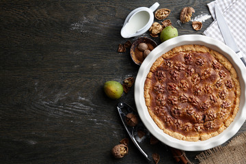 Traditional walnut pie, spices, nuts and nutcracker on dark wooden table, top view