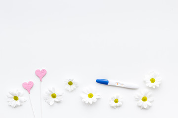 Joy of long-awaited pregnancy. Pregnancy test with two stripes near flowers on white background top view copy space