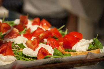 Caprese salad of fresh Italian mozzarella, sliced red tomatoes and green basil and arugula, salad on bruschetta from organic bread, Italian appetizer
