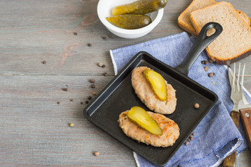Appetizing appetizer. Homemade meat cutlets with pieces of salted cucumber on a black cast-iron frying pan on an old wooden table. 