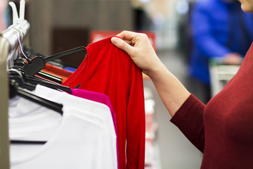 girl in clothing store chooses sweatshirt on hanger. Woman shopping.