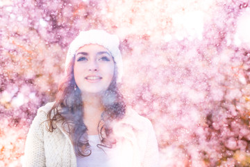 A girl in a warm hat and a knitted sweater, on a pink background with glare. Glamor and youth, snow or flowering. Aspiration, look up, smile, success and love. An inspiration and a positive attitude. 