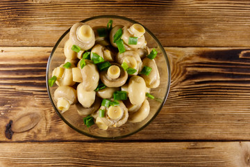 Glass bowl with pickled champignons. Marinated mushrooms on wooden table