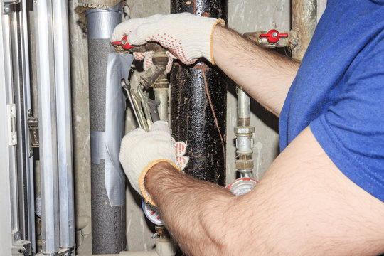 The plumber in white gloves with wrenches repairs the pipes in the plumbing unit. Repair of pipes, valves, water meters