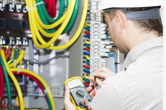 engineer makes measurements with multimeter in electrical cabinet. Electrician with tester in the hands on background of electrical panel. Adjustment of the electrical fuse box
