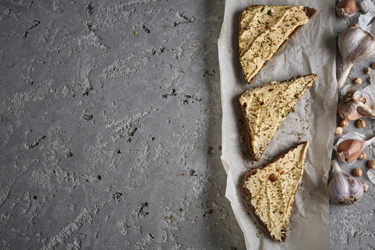 three slices of whole wheat bread with hummus, chickpea and garlic on the grey concrete backdrop