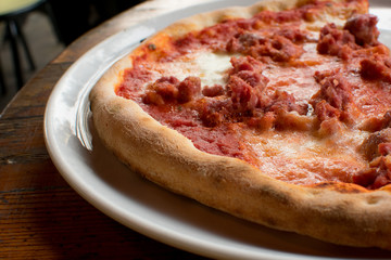 pizza with meat, mozzarella, tomato sauce and olive oil on a white plate.