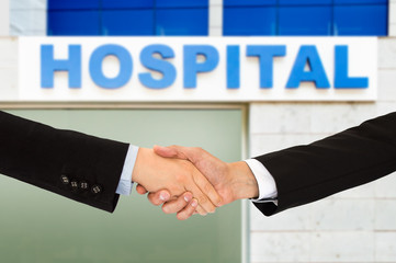 Cropped shot of a doctor shaking the hand of a patient next hospital building