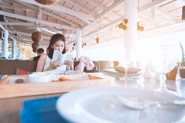 Beautiful asian woman has smile and hides his face behind a book with relaxing time on the holiday and vacation in the evening at restaurant nearby the sea and beach.