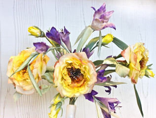 Yellow peonies and irises in a white vase. Artificial silk flowers in the interior