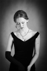 Fototapeta premium Girl in evening dress taking off long gloves. Black and white portrait in studio