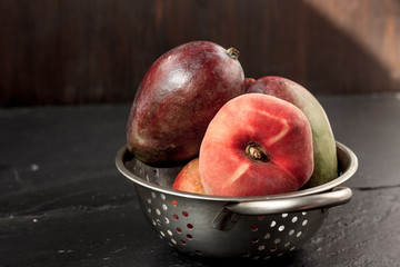 Mango and peach fruits in metal colander