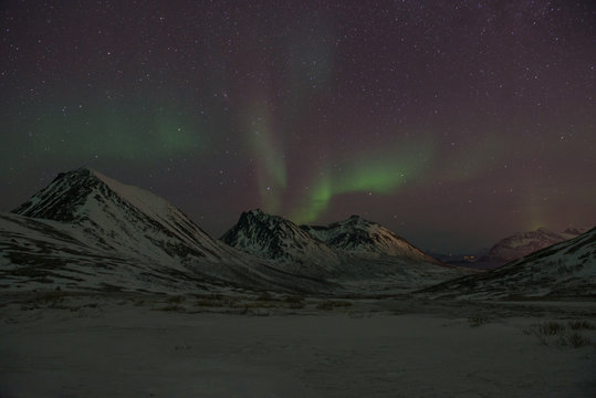 Bright green Northern Light (Aurora Borealis) lighting up the dark skies above the mountains, Tromsø, Norway