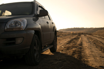 Fototapeta na wymiar SUV in the field at sunset, car and a road, headlight, warm, dusty evening