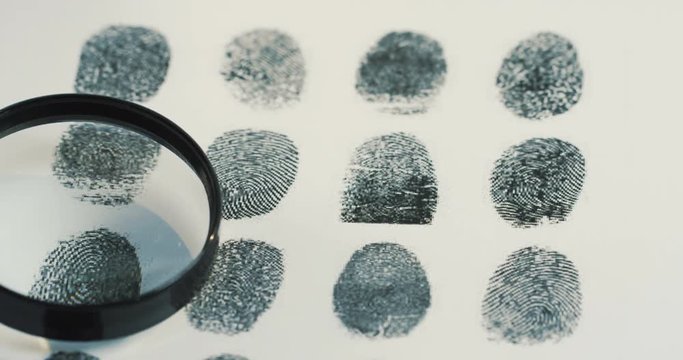 Macro of the female hand investigating fingerprints with a magnifying glass. Close up
