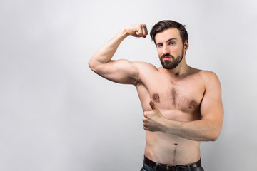 Obraz premium A picture of a topless guy standing at white wall and showing a play of the muscles om his right hand. He looks incredible and powerful. Cut view. Isolated on white background