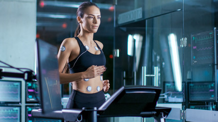 Beautiful Woman Athlete Runs on a Treadmill with Electrodes Attached to Her Body, Female Physician Uses Tablet Computer and Controls EKG Data Showing on Laboratory Monitors.