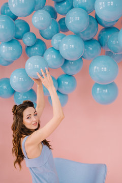 A girl of small stature in a pink room is playing with blue balls
