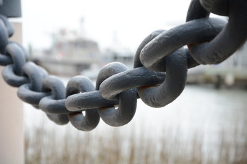 Huge black anchor chain hanging between two posts in a shipyard