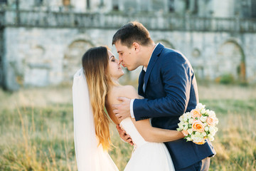 Beautiful wedding couple poses before an old ruined castle in the rays of evening sun