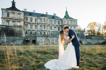 Beautiful wedding couple poses before an old ruined castle in the rays of evening sun