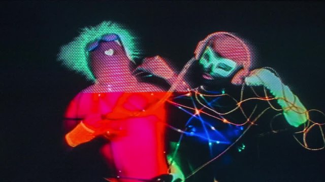 glow raver man and woman tied up together with led cables, filmed in fluorescent clothing under UV black light. this version has overlayed video distortion and glitch effects