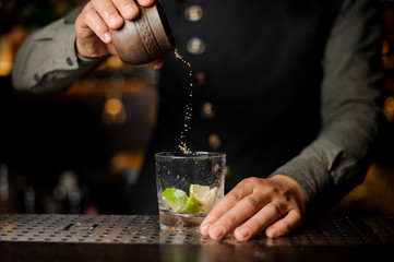 Bartender adding cane sugar into the cocktail glass. Process of making Caipirinha cocktail