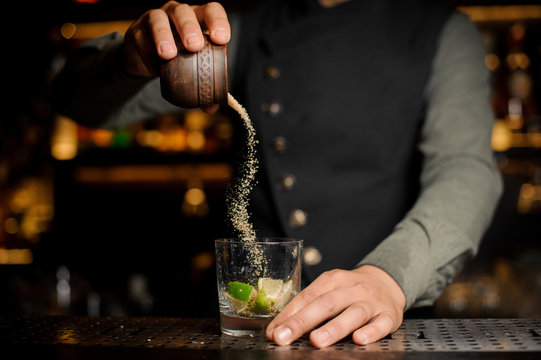 Barman adding cane sugar into the cocktail glass with lime. Process of making Caipirinha cocktail